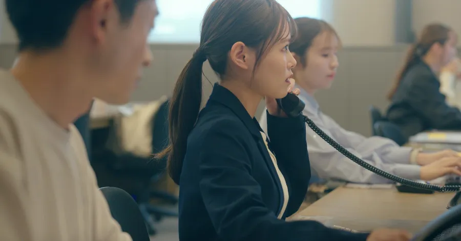 写真:机で電話をとっている女性社員。他にも同じように電話を受ける社員が複数人座っている。