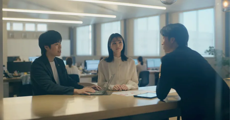 写真:ミーティングテーブルで、PCやタブレットを広げて会議をしている3名の社員